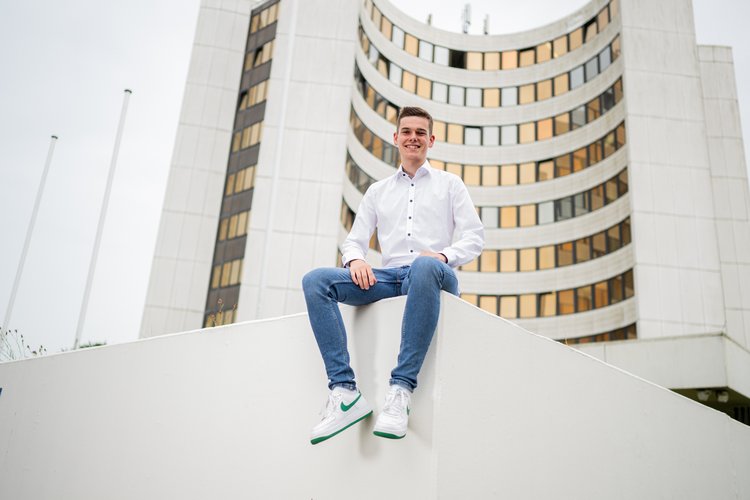 Männliche Person sitzt auf einer Mauer vor dem Kreishaus-Gebäude
