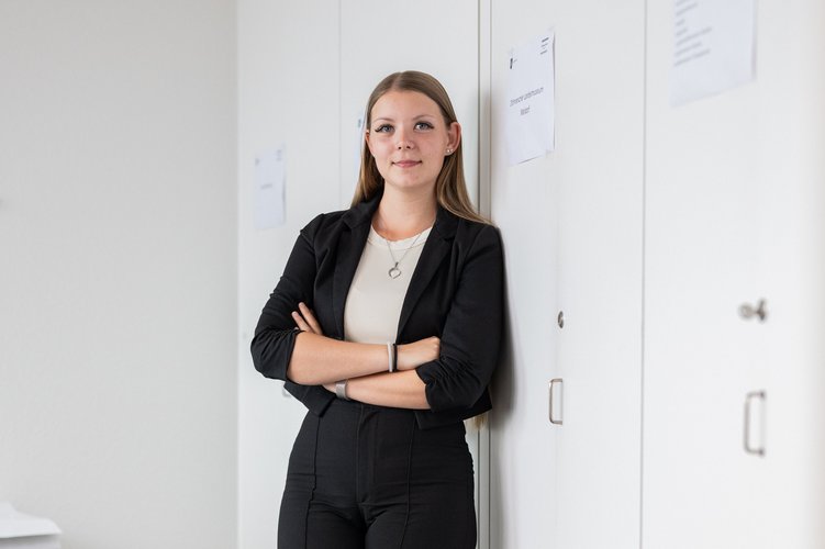Junge Frau lehnt an einem Schrank im Büro und schaut freundlich in die Kamera