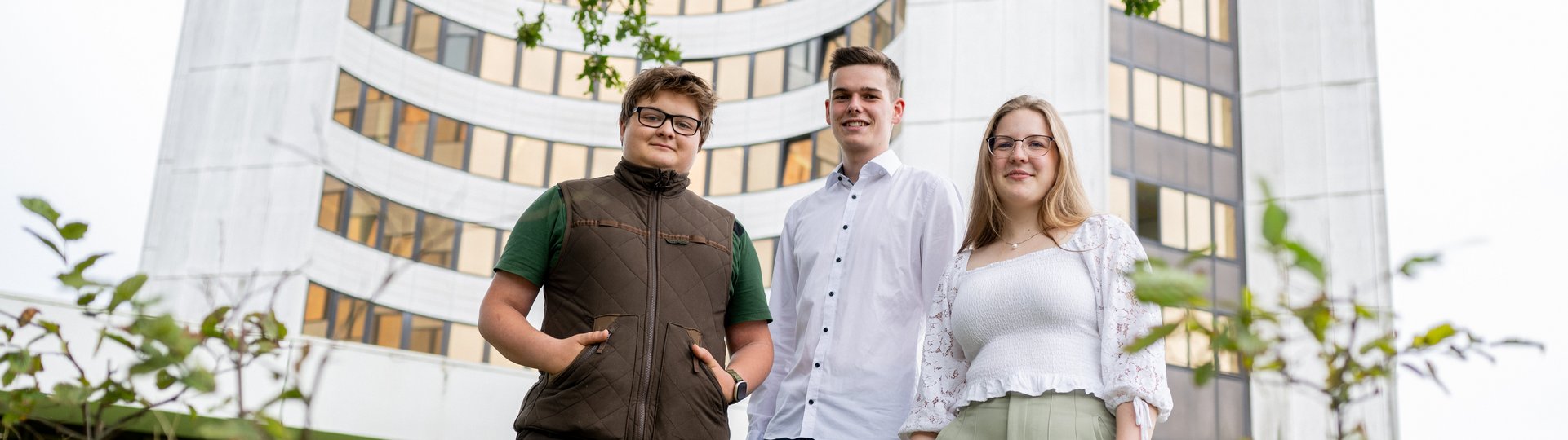 Drei Auszubildende, zwei Männer und eine Frau, stehen vor dem Kreishausgebäude